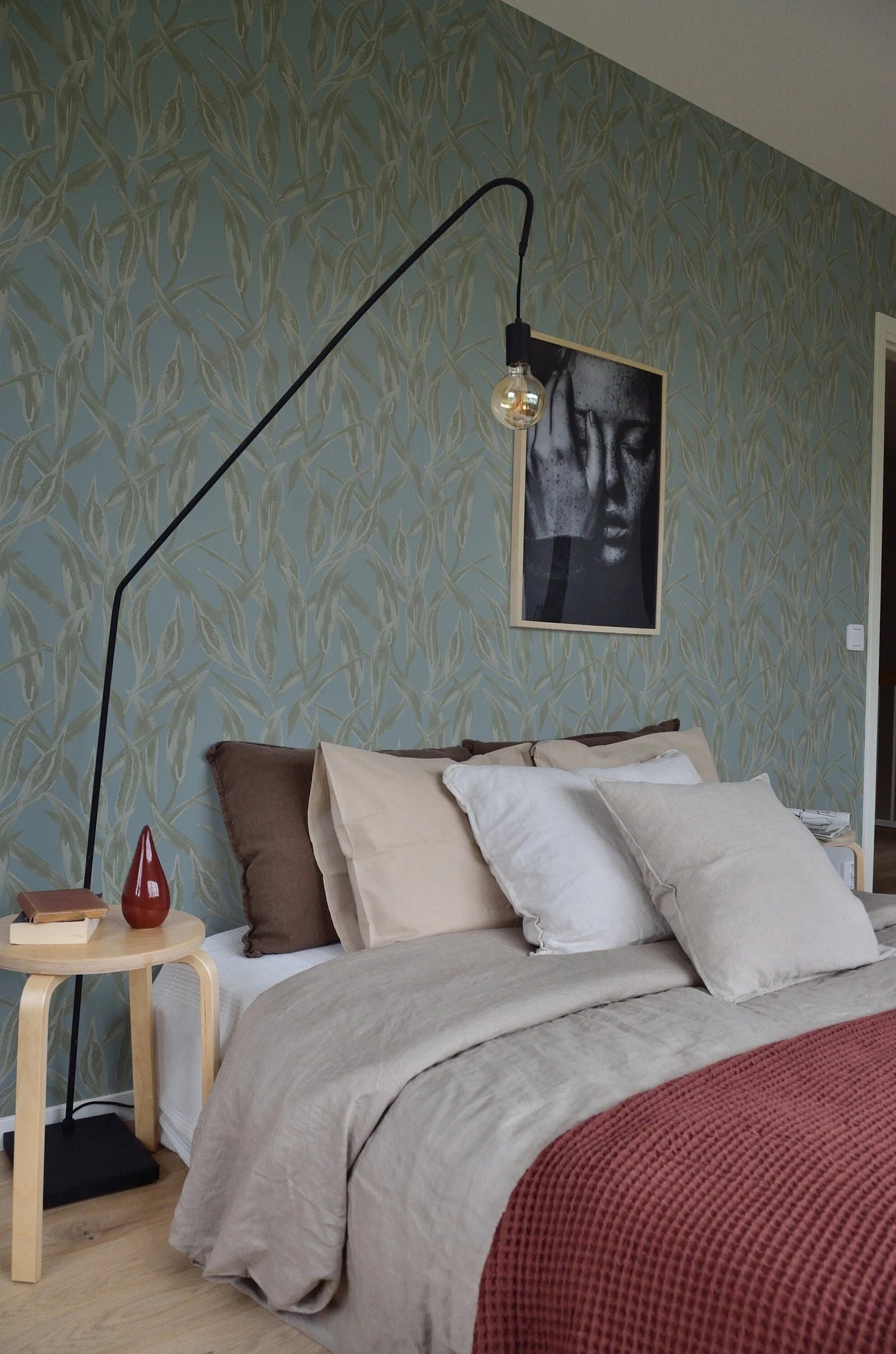 a cozy bedroom with a large bed, a nightstand, and a framed artwork on the wall. The room has a green and white color scheme, and the bed is adorned with a red blanket and multiple pillows.
