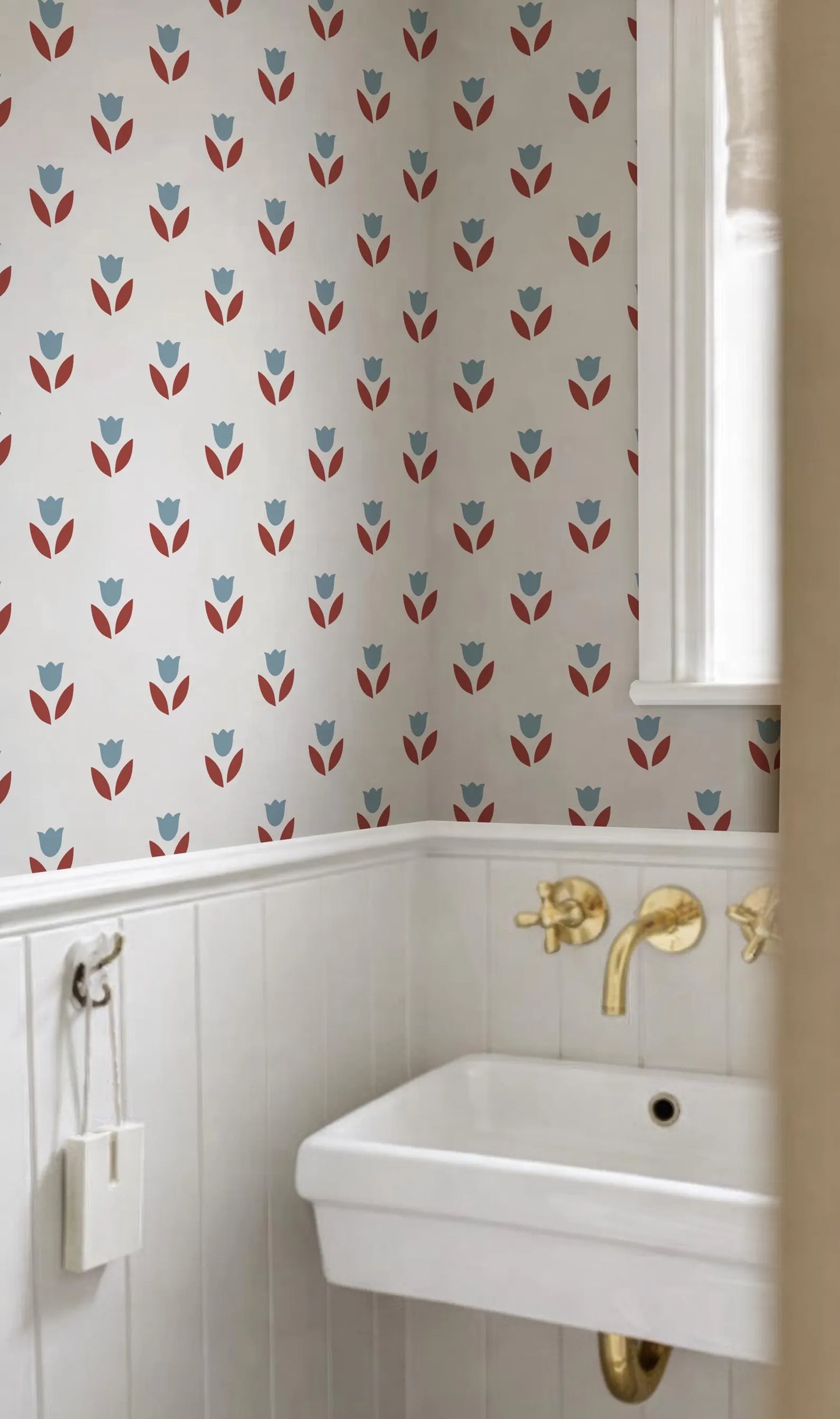 a bathroom with a white sink and a wall with a pattern of red and blue flowers. The sink has gold faucets, and there is a window in the background.