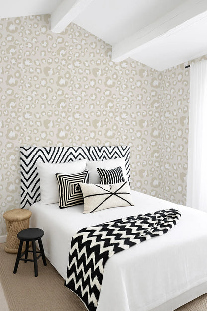 a bedroom with a bed, a stool, and a patterned wallpaper. The bed has a black and white zigzag patterned headboard and a white comforter. The stool is positioned next to the bed. The wallpaper has a leopard print pattern.