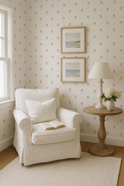 A cozy corner of a room with a white armchair, a small side table with a lamp and a vase of flowers, and two framed pictures on the wall.