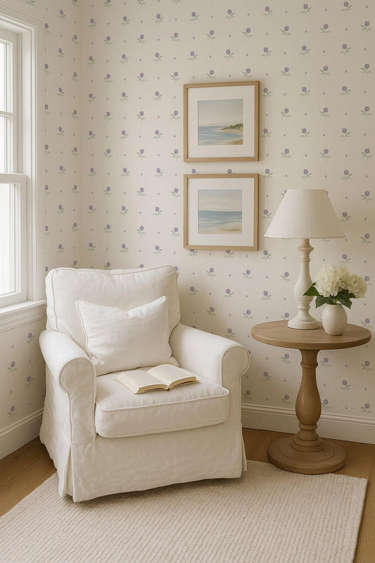 A cozy corner of a room with a white armchair, a small side table with a lamp and a vase of flowers, and two framed pictures on the wall.