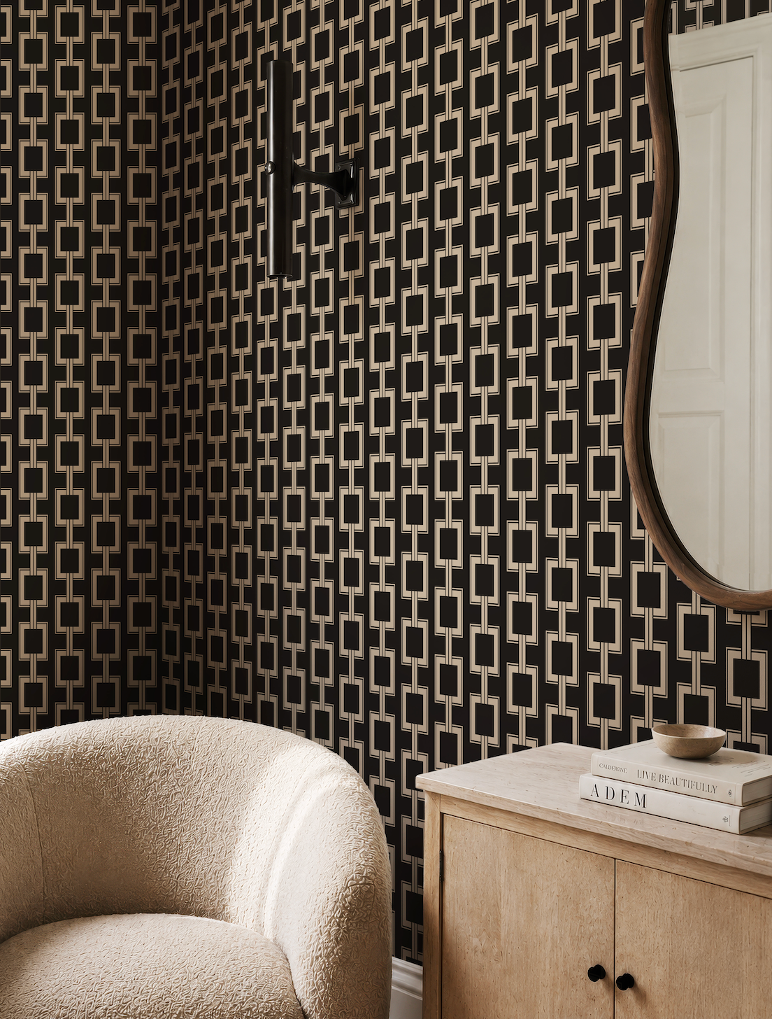 a modern living room with a black and white geometric wallpaper pattern, a curved mirror, a white armchair, and a wooden sideboard with a mirror above it.
