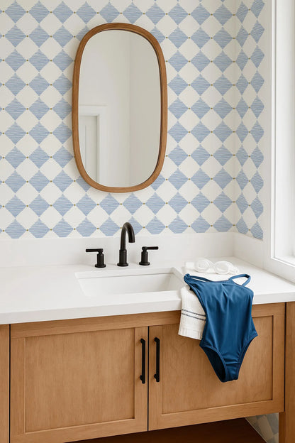 a bathroom with a white sink, a mirror above it, and a blue and white patterned wallpaper. There is a blue swimsuit hanging on the side of the sink.