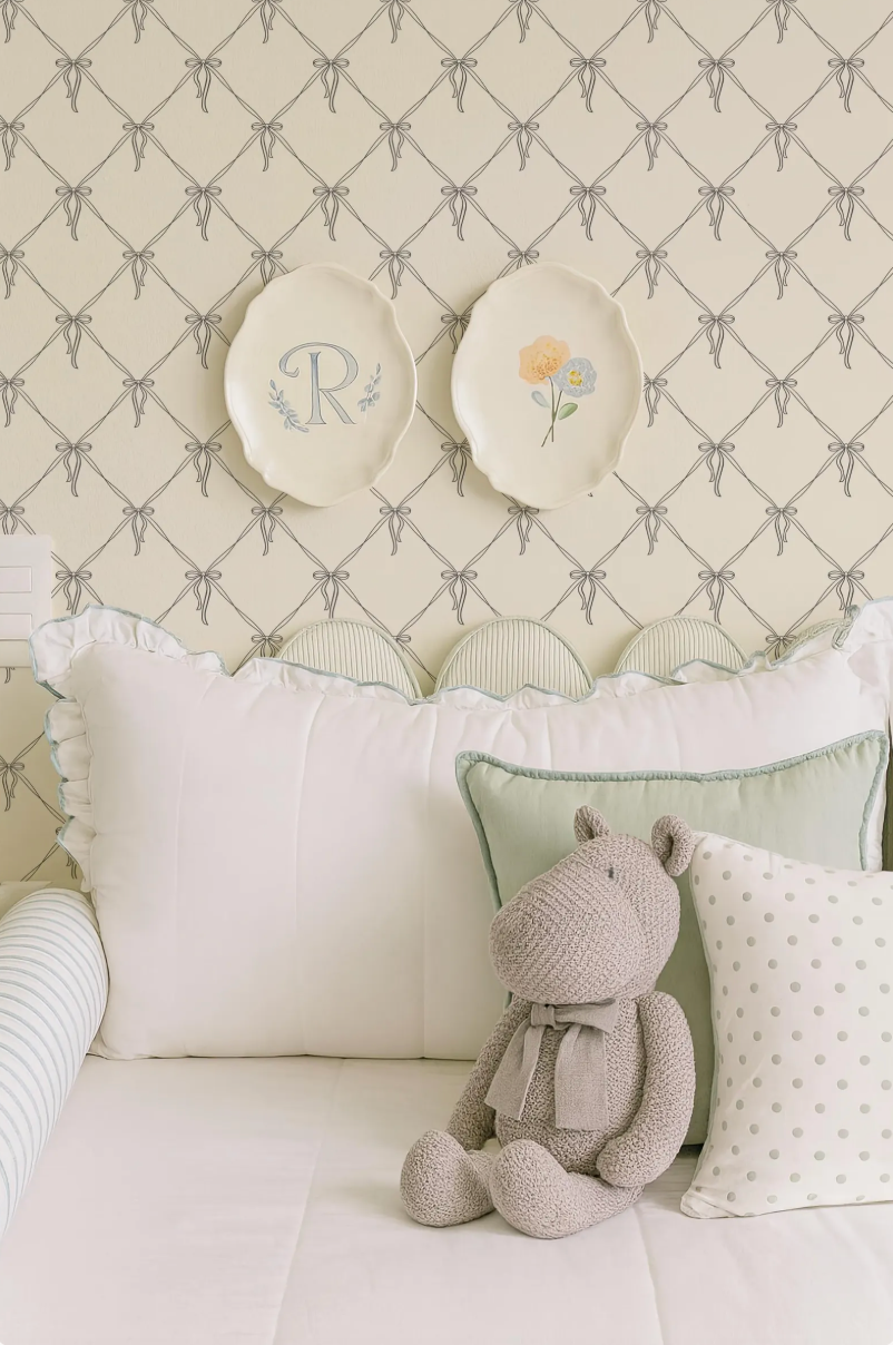 a cozy bedroom scene with a plush teddy bear sitting on a bed, surrounded by decorative pillows and a wall with a patterned wallpaper.