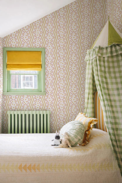a cozy bedroom with a bed, a window with a yellow shade, and a green and white checkered canopy. The room has a patterned wallpaper and a green radiator. A stuffed animal is resting on the bed.