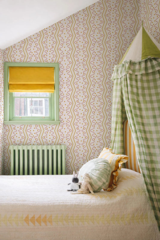 a cozy bedroom with a bed, a window with a yellow shade, and a green and white checkered canopy. The room has a patterned wallpaper and a green radiator. A stuffed animal is resting on the bed.