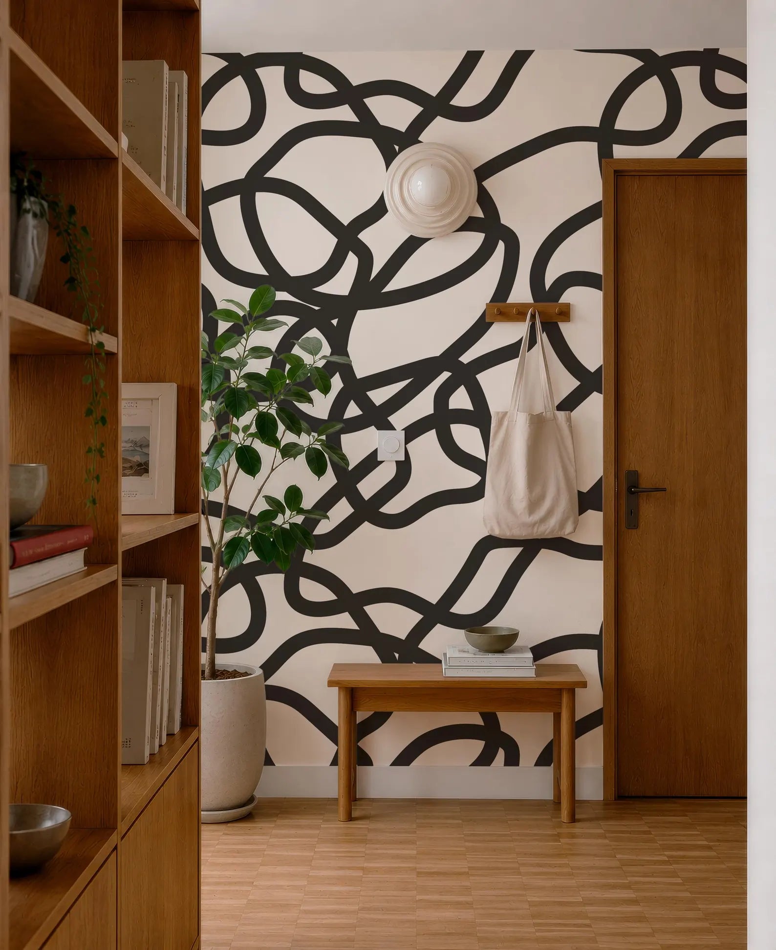 a modern and stylish interior design with a black and white abstract pattern on the wall behind a wooden bench. The room also includes a bookshelf, a potted plant, and a wooden door.