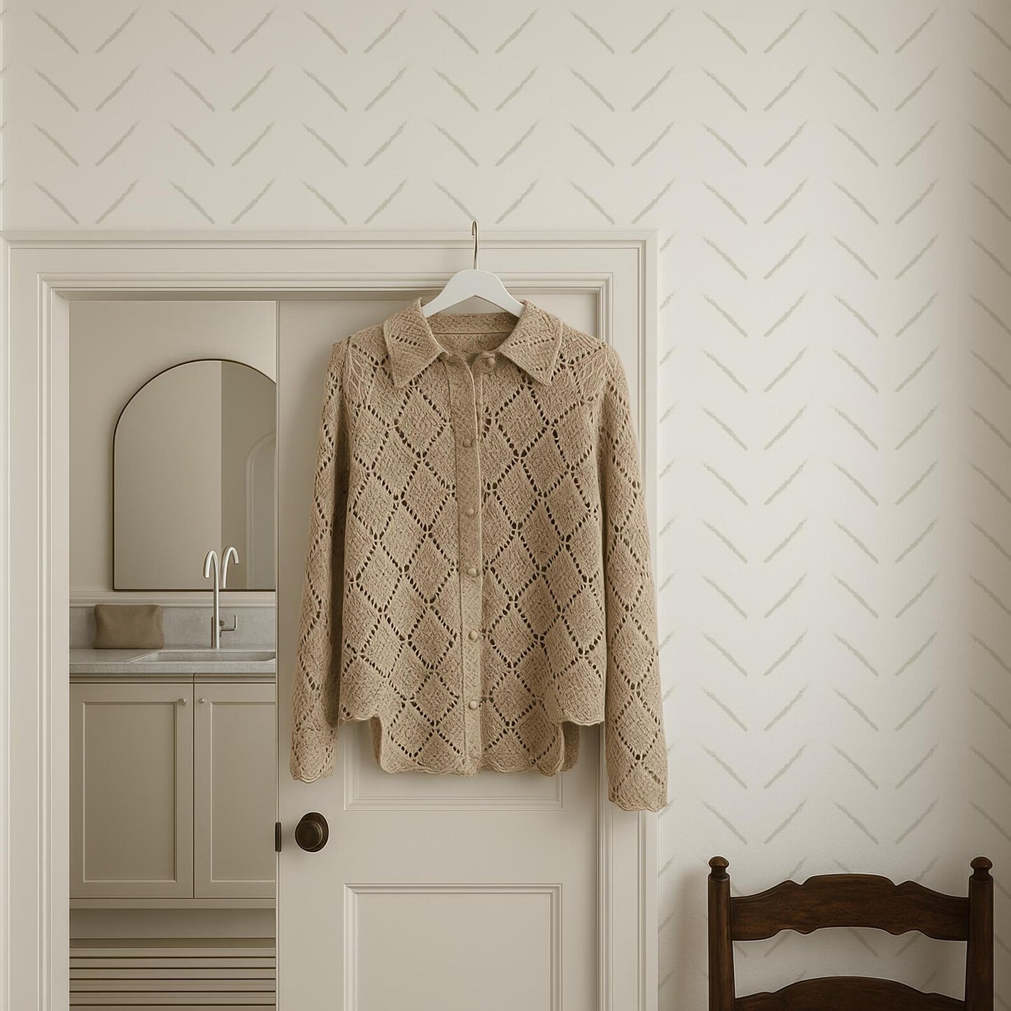 a beige knitted sweater hanging on a white door, with a wooden chair visible in the background.