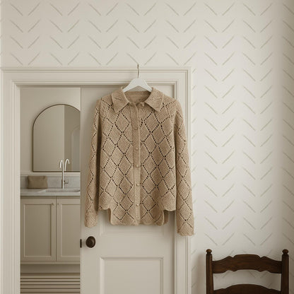 a beige knitted sweater hanging on a white door, with a wooden chair visible in the background.