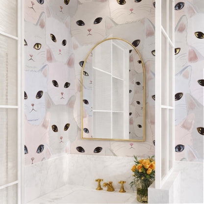 a bathroom with a white sink and a gold faucet, and a mirror above it. The wall behind the sink is covered in a repeating pattern of cat faces in various colors and sizes. There is also a vase of flowers on the counter next to the sink.