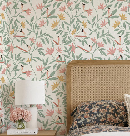 a bedroom setting with a floral wallpaper pattern, a wooden headboard, a lamp, and a vase of pink flowers on a nightstand.
