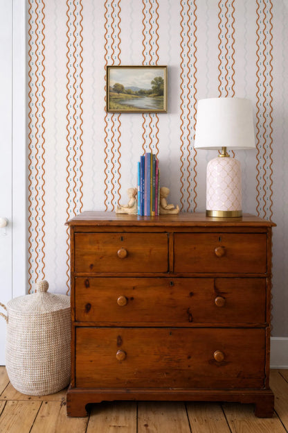 a wooden dresser with a lamp, a basket, and a framed landscape painting on the wall.