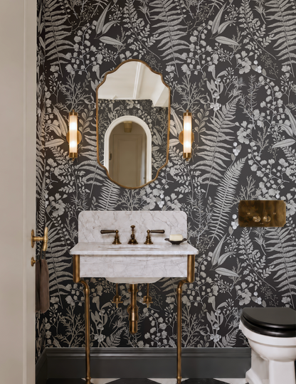 a bathroom with a white marble sink, a gold faucet, and a black and white floral wallpaper. The bathroom also includes a toilet and two wall sconces.