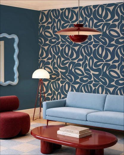 a modern living room with a blue sofa, a red armchair, and a red coffee table. The room has a patterned blue and white wall, and a red pendant light hangs above the sofa. There is also a white floor lamp in the corner of the room.