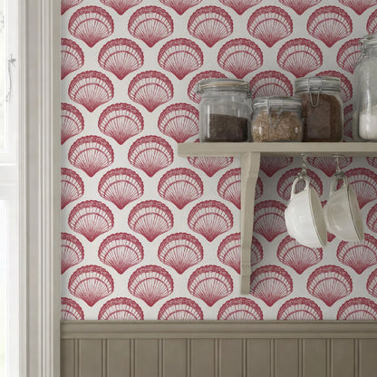 a kitchen setting with a wallpapered wall adorned with a repeating pattern of red and white seashells. On the wall, there is a shelf holding various jars and containers, including two jars of spices and two white mugs.