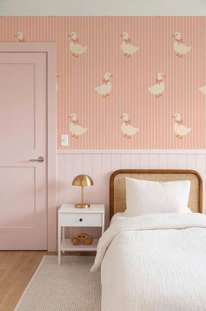 a bedroom with a pink wall featuring a repeating pattern of ducks. The room includes a bed with a white comforter, a nightstand with a lamp, and a door.
