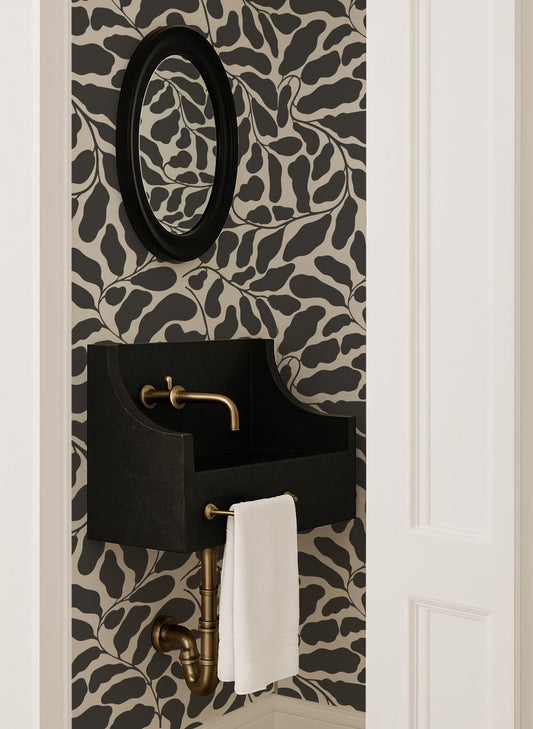 a bathroom with a black sink and a gold faucet, set against a black and white leaf-patterned wallpaper. A white towel is hanging on the sink.