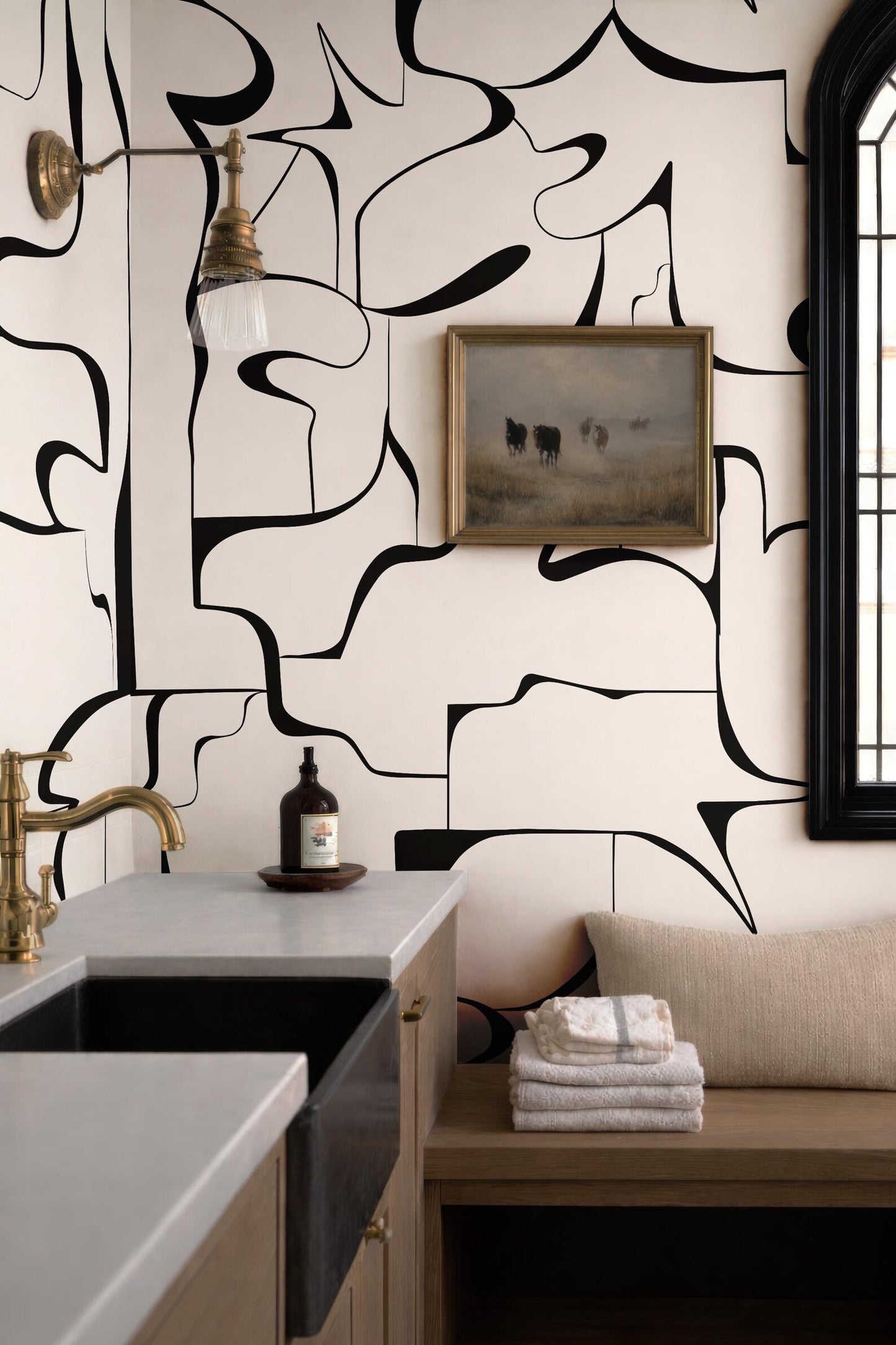 a modern bathroom with a black and white abstract design on the walls, a sink, a wooden bench, and a framed artwork depicting cows.