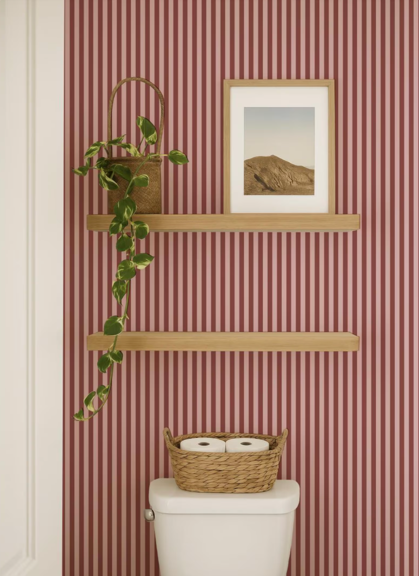 a bathroom with a toilet, a shelf with a plant and a picture, and a basket of toilet paper on the tank.
