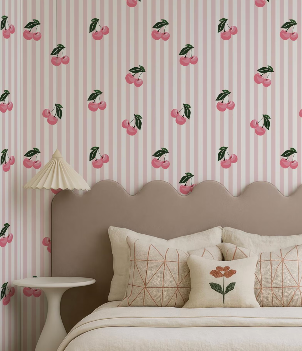 a bedroom with a bed, a headboard, and a wallpapered wall with a repeating pattern of pink and green cherries.