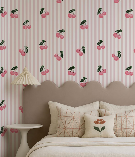 a bedroom with a bed, a headboard, and a wallpapered wall with a repeating pattern of pink and green cherries.