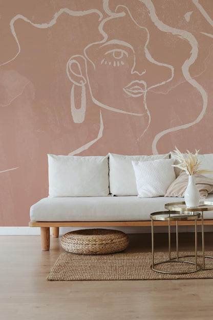 a living room with a white sofa, a woven rug, and a coffee table with a vase of flowers. The walls are painted in a peach-colored hue, and there is a large abstract drawing of a woman's face on the wall.
