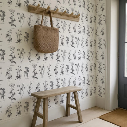 a wooden bench situated in a room with a wall adorned with a repeating pattern of black and white floral designs. Above the bench, there is a wooden coat rack holding a woven bag.
