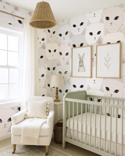 a nursery room with a white crib, a white armchair, and a wallpapered wall featuring a repeating pattern of cat faces.
