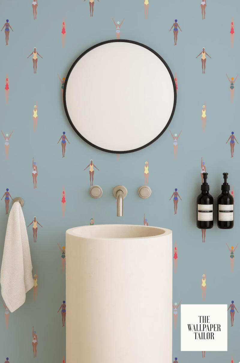a bathroom with a white sink, a round mirror, and a towel rack. The wall behind the sink has a pattern of colorful swimming figures.