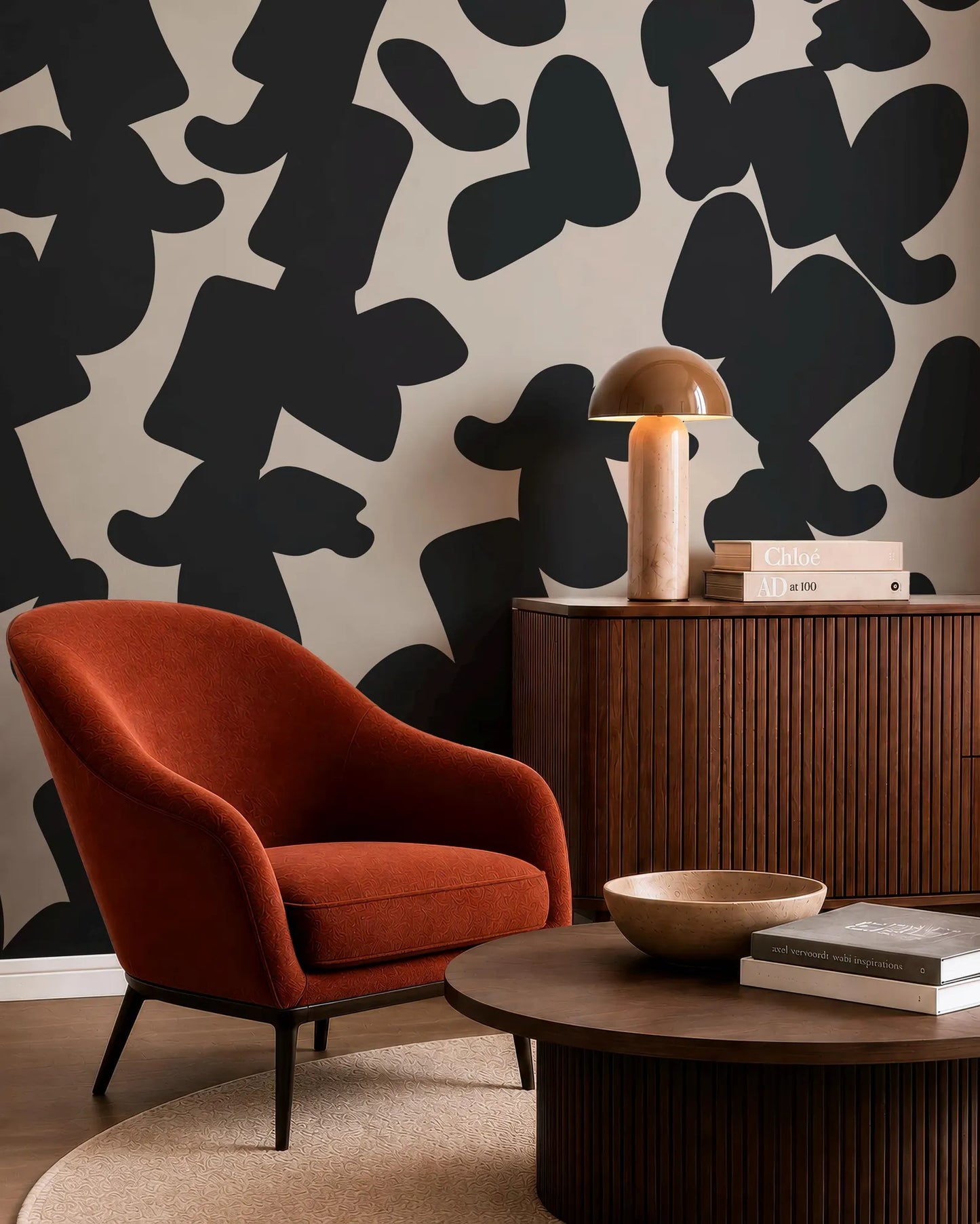 a modern living room with a red armchair, a wooden side table with a lamp, and a wooden coffee table with a bowl on it. The wall behind the furniture has a black and white abstract pattern.
