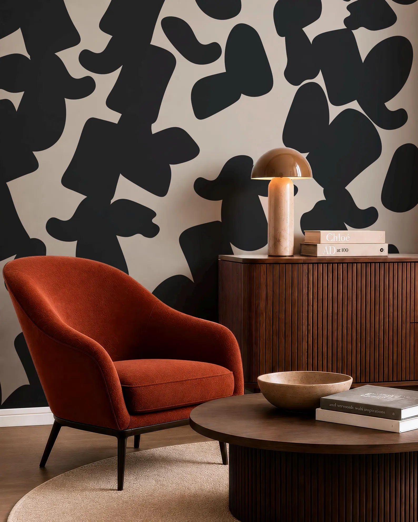a modern living room with a red armchair, a wooden side table with a lamp, and a wooden coffee table with a bowl on it. The wall behind the furniture has a black and white abstract pattern.
