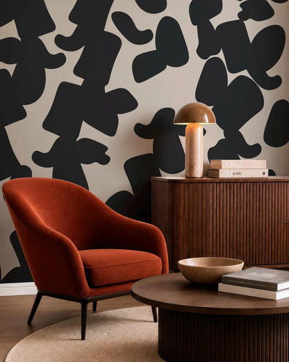 a modern living room with a red armchair, a wooden side table with a lamp, and a wooden coffee table with a bowl on it. The wall behind the furniture has a black and white abstract pattern.