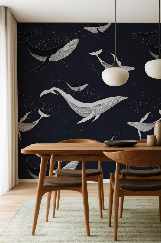 a modern dining room with a dark blue wall adorned with a whimsical design of white and black whale silhouettes. The room is furnished with a wooden dining table and chairs, and two hanging pendant lights illuminate the space.