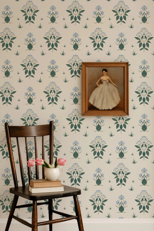 a wooden chair with pink flowers in a white vase, a framed painting of a woman in a white dress, and a bookshelf with books. The background has a floral wallpaper pattern.