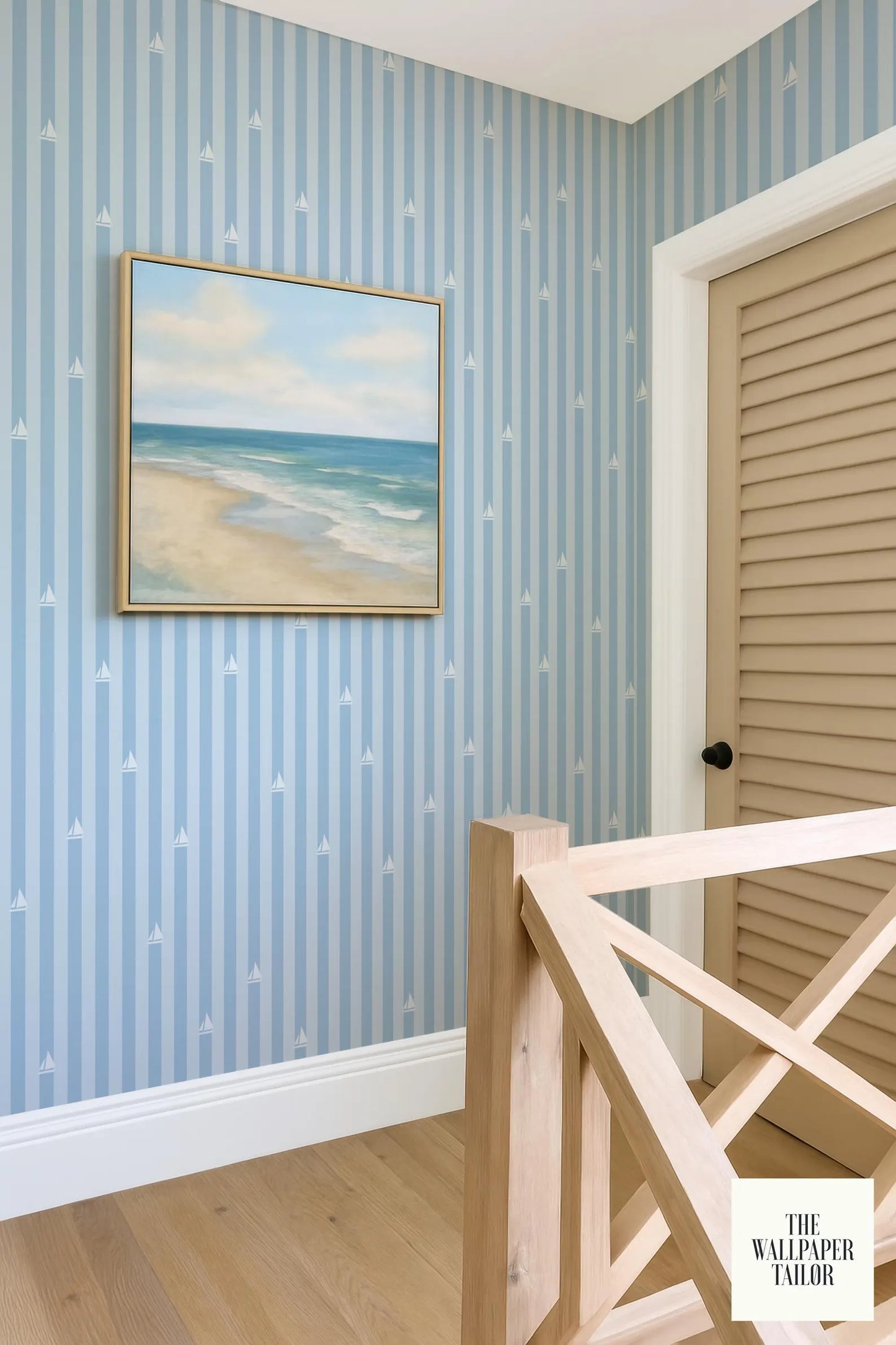 a coastal-themed room with a framed painting of a beach scene on the wall, a wooden staircase, and a door with a wooden frame.