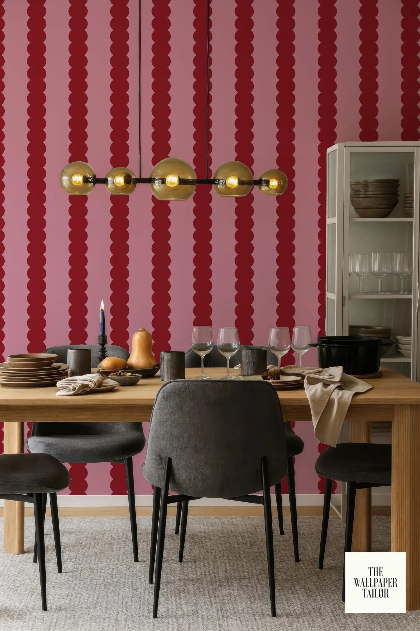 a dining room with a wooden table set for four, featuring a black chair, wine glasses, and a bowl. The walls are painted in a bold red and pink color scheme, and a chandelier hangs above the table.