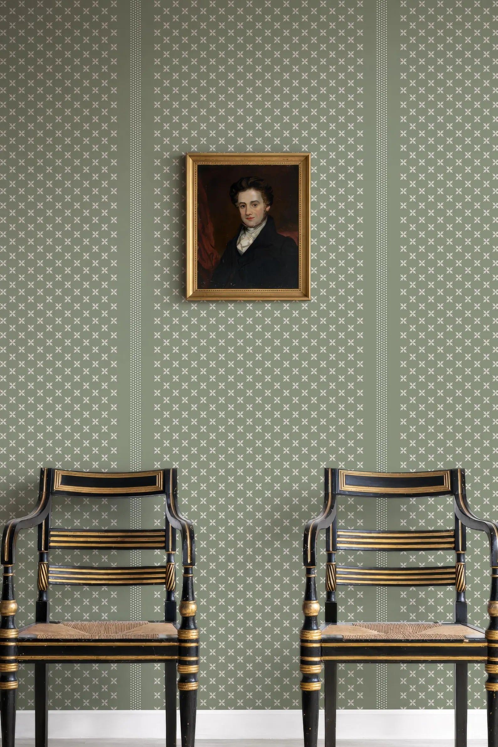 a portrait of a man hanging on a wall, with two black chairs positioned in front of it.