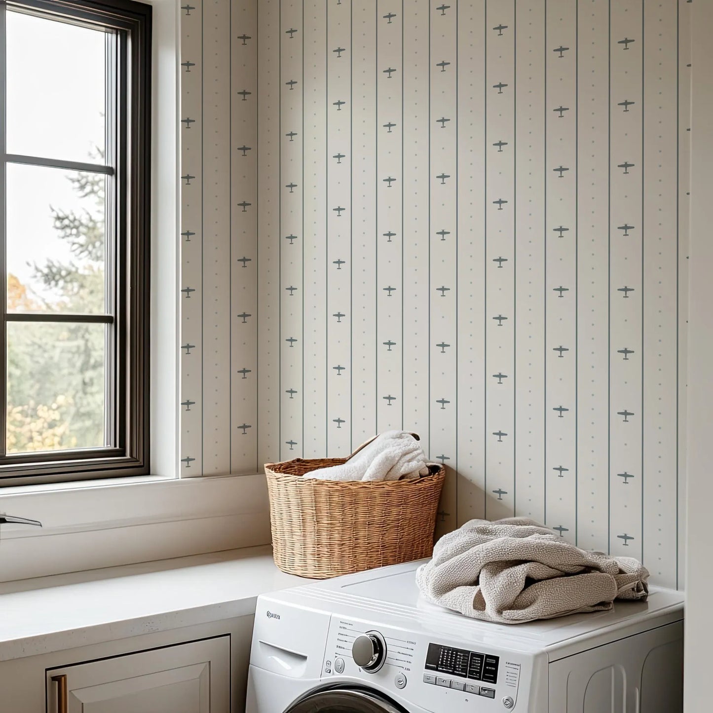 a laundry room with a washing machine, a basket of folded towels, and a window overlooking a natural outdoor scene.
