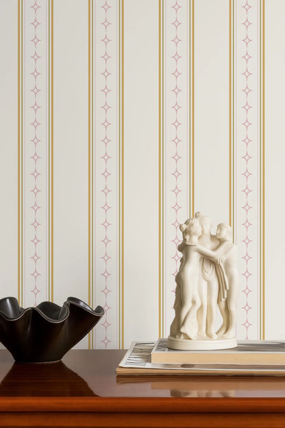 a wooden table with a black bowl, a white figurine, and a stack of books. The table is set against a striped wallpaper with a repeating pattern of pink and gold lines.