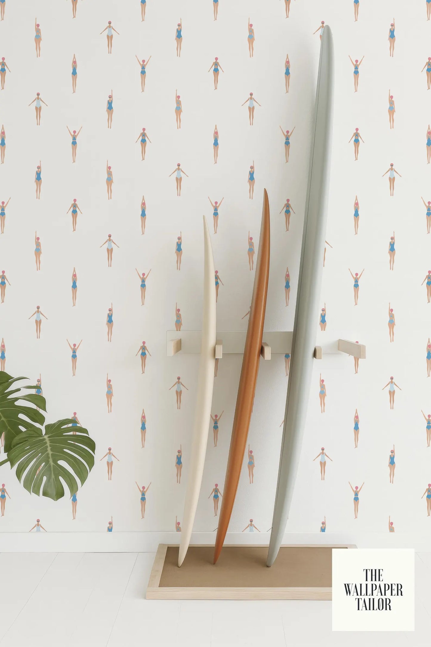 a wallpapered wall with a repeating pattern of swimming figures, and there are three surfboards standing upright against the wall.