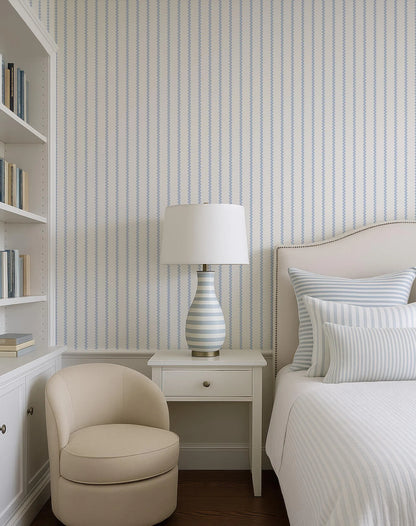 a cozy and well-organized bedroom with a bed, a white armchair, a white side table with a lamp, and a bookshelf filled with books.