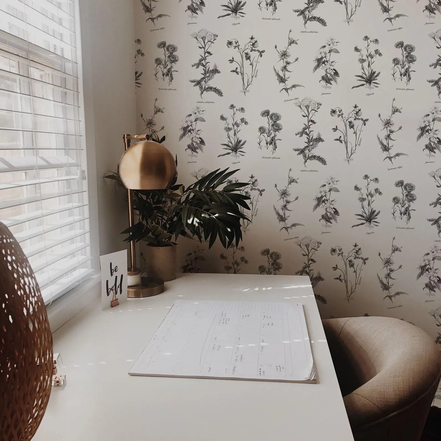 a white desk with a lamp, a plant, and a calendar, set against a wall with a floral wallpaper.
