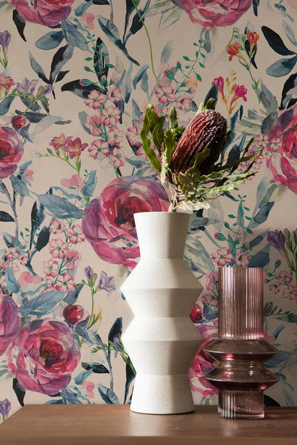 a white vase with a bouquet of flowers and a pink vase with a purple flower on a wooden surface, set against a floral wallpaper background.