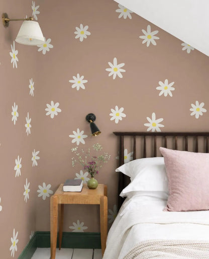 a cozy bedroom with a bed, a nightstand, and a lamp. The walls are decorated with a pattern of white daisies, and the room has a warm, inviting atmosphere.