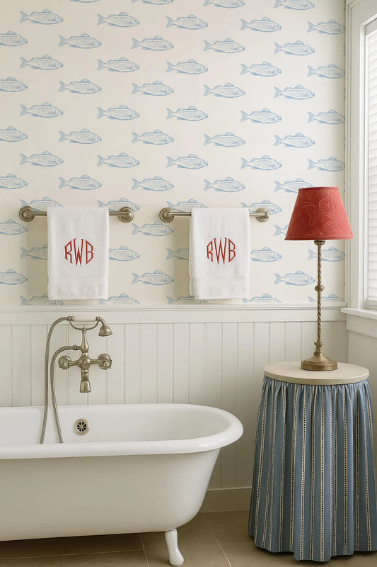 a bathroom with a clawfoot bathtub, a towel rack with two towels, a red lamp, and a blue and white fish wallpaper.