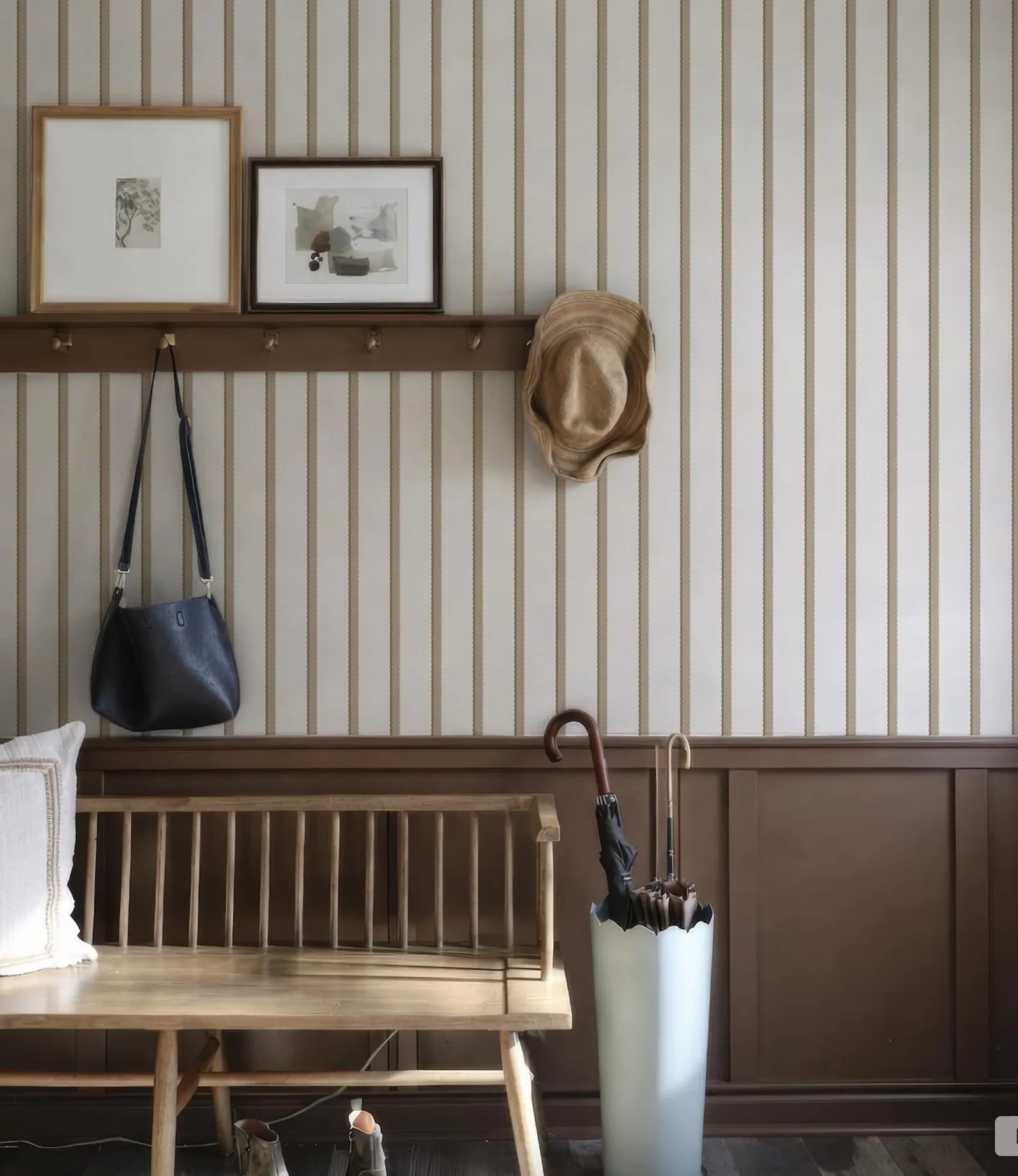 a wooden bench, a shelf with framed pictures, a hat hanging on the wall, and an umbrella stand with an umbrella.