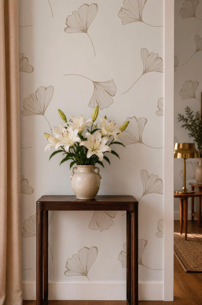 a wooden table with a vase of white lilies placed on it, set against a wall with a repeating pattern of gilt leaf designs.