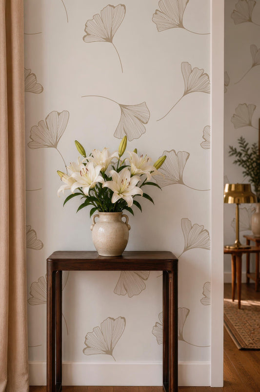 a wooden table with a vase of white lilies placed on it, set against a wall with a repeating pattern of gilt leaf designs.