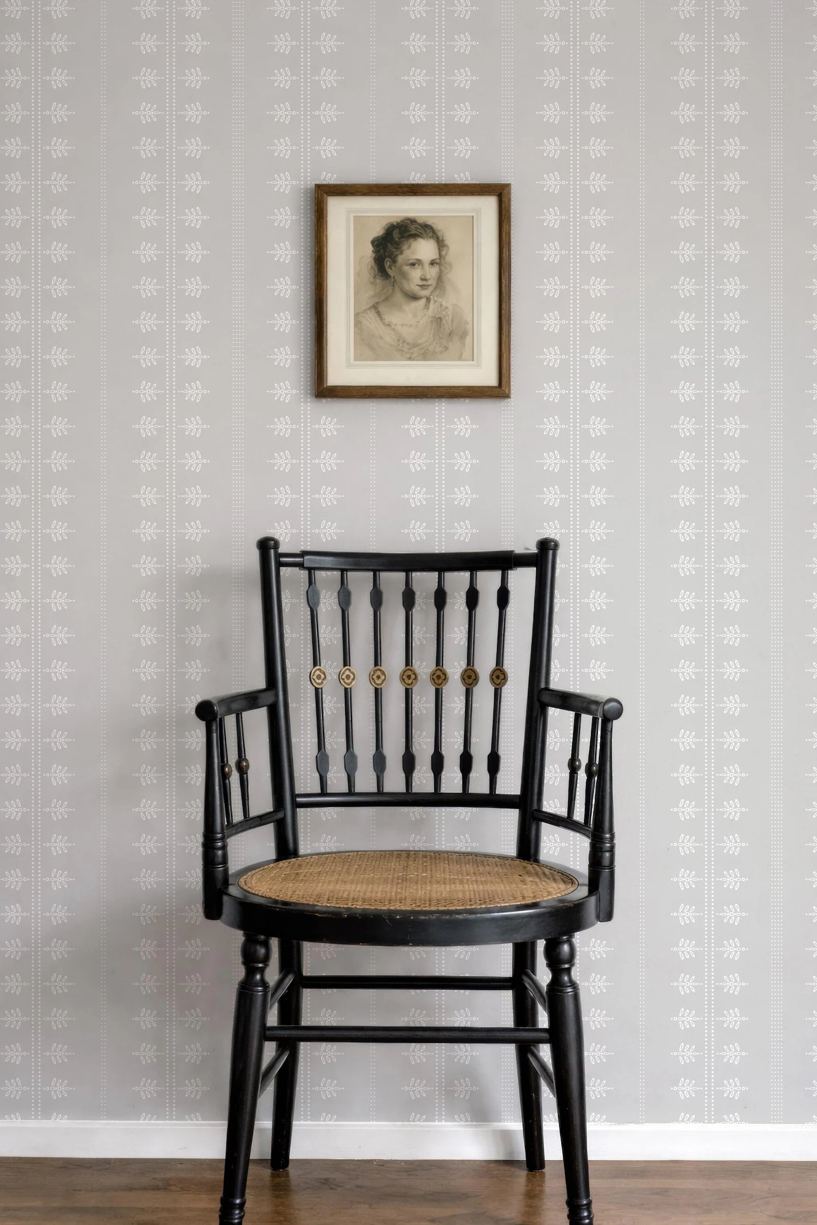 a black wooden chair with a woven seat, positioned against a gray wall with a framed portrait hanging above it.