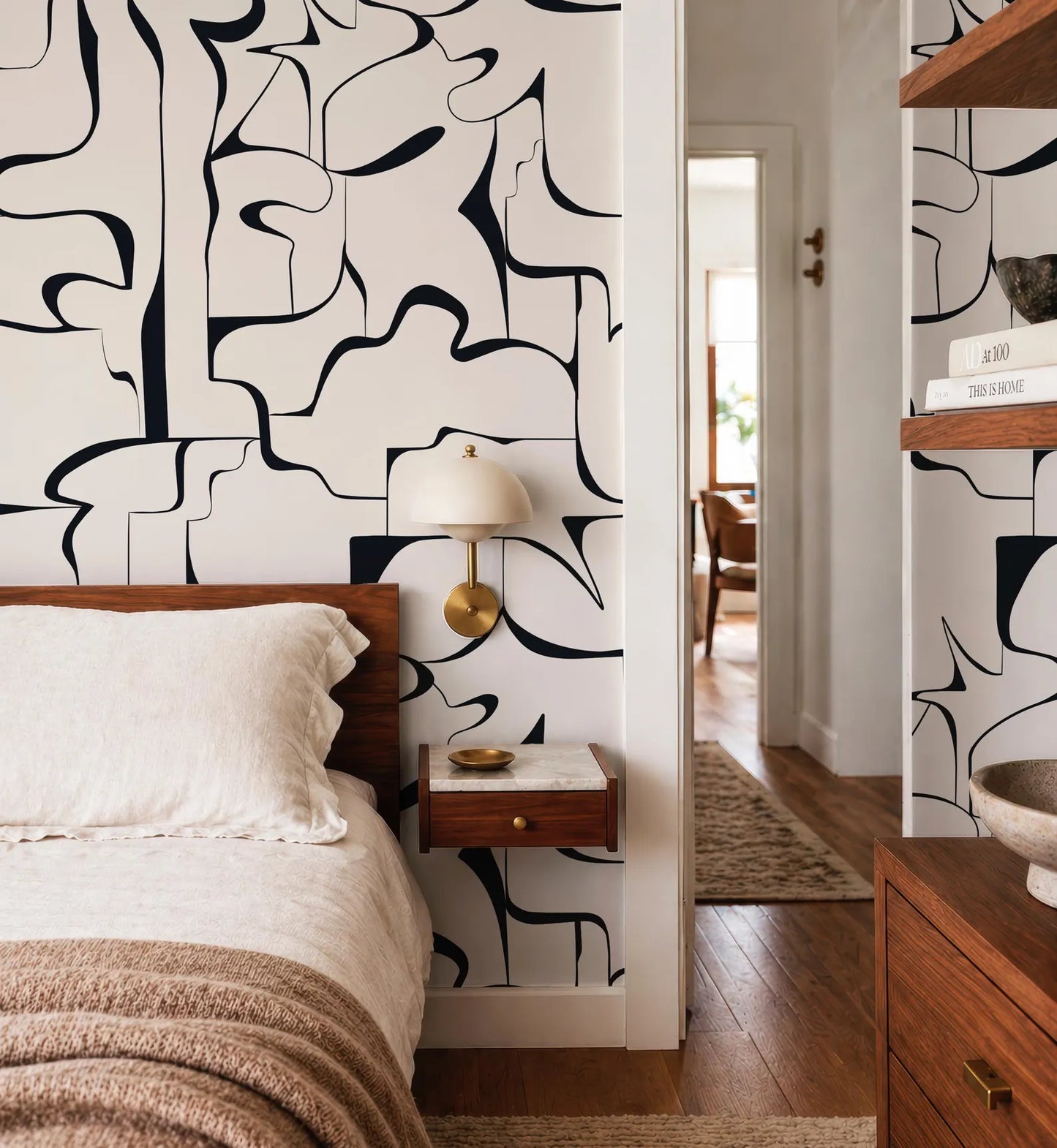 a modern bedroom with a large abstract black and white pattern on the wall behind the bed. The room has a wooden bed frame and a wooden nightstand with a lamp. The overall design and decor create a stylish and contemporary atmosphere.